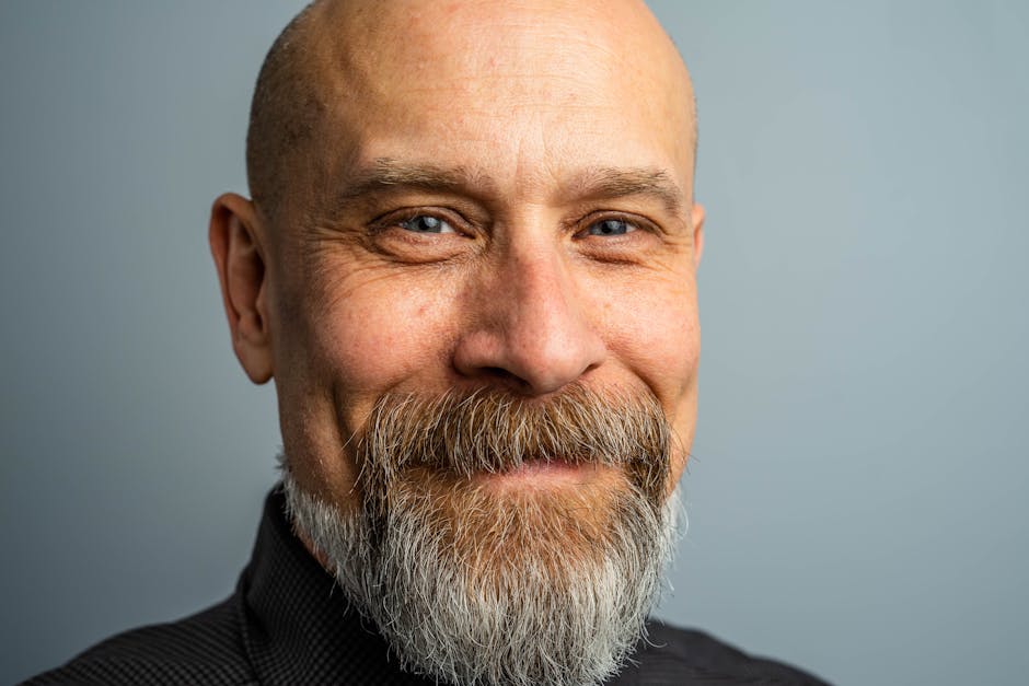 Close-up portrait of a mature bald man with a full beard, exuding confidence and style in a professional studio setting.