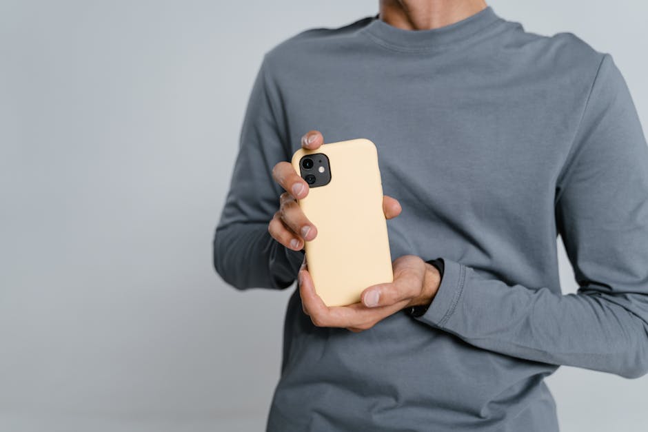 Close-up of a man holding a smartphone with a yellow case, wearing casual attire, shot in a studio.