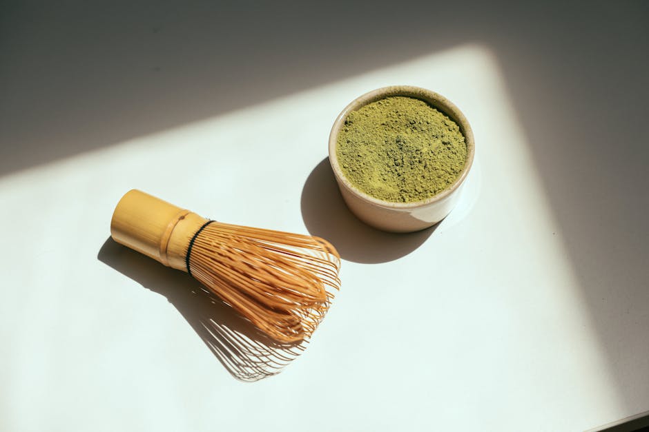 Minimalist composition featuring matcha powder and bamboo whisk in sunlight.