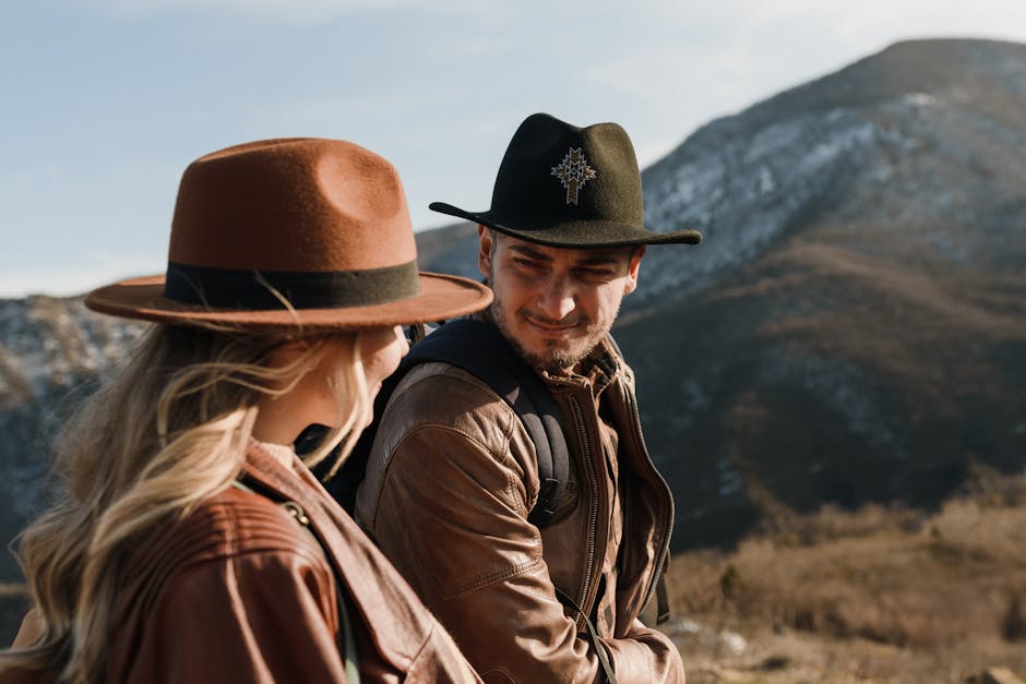 A couple in stylish hats and jackets hiking in a scenic mountain landscape during summer.