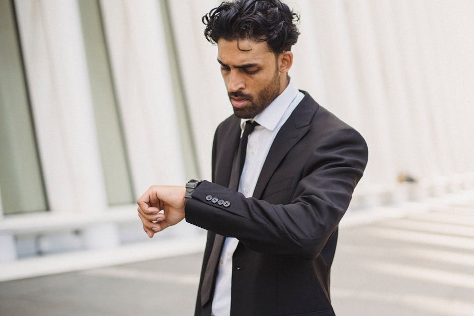 A businessman in corporate attire checking time on his smartwatch outdoors.