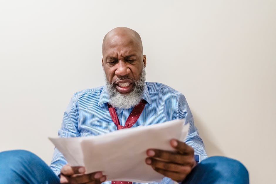 A bearded man intently reviews documents, expressing stress and concern indoors.