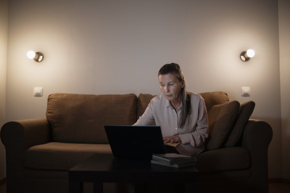 A senior woman focused on her laptop in a cozy, well-lit living room setting.