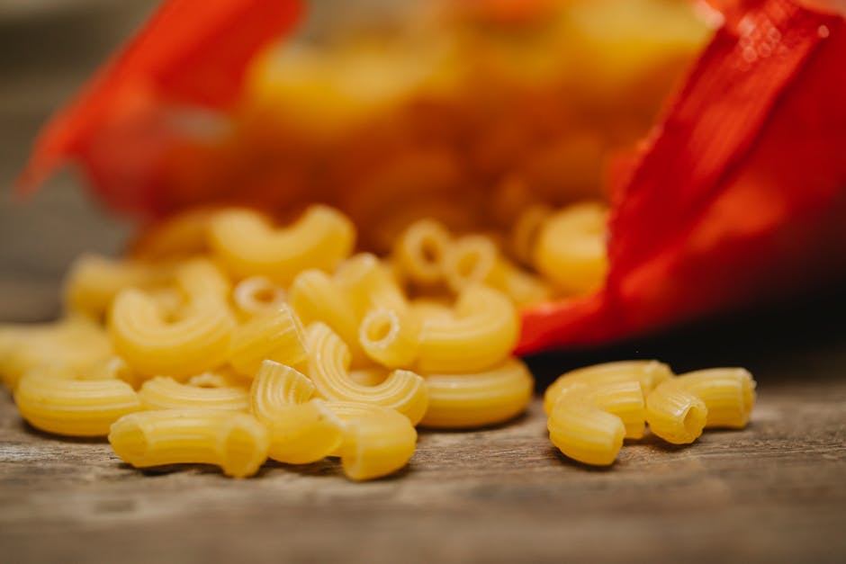 Close-up of uncooked pipe rigate pasta spilled from a red bag onto a rustic wooden table.