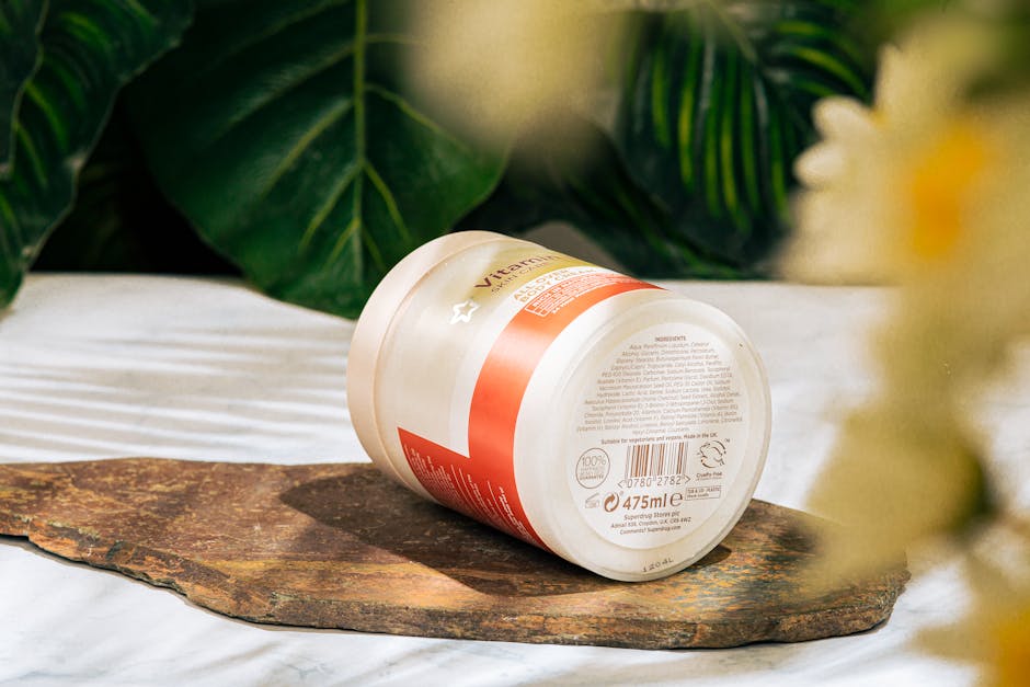 Skincare product jar on a marble surface surrounded by lush green leaves.