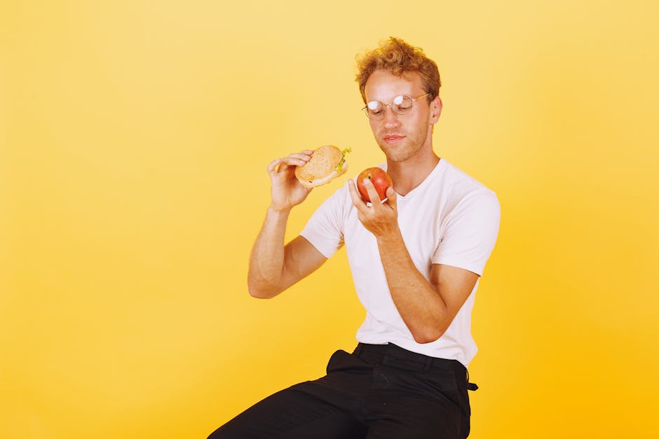 Man in white shirt holding a burger and apple on yellow background.