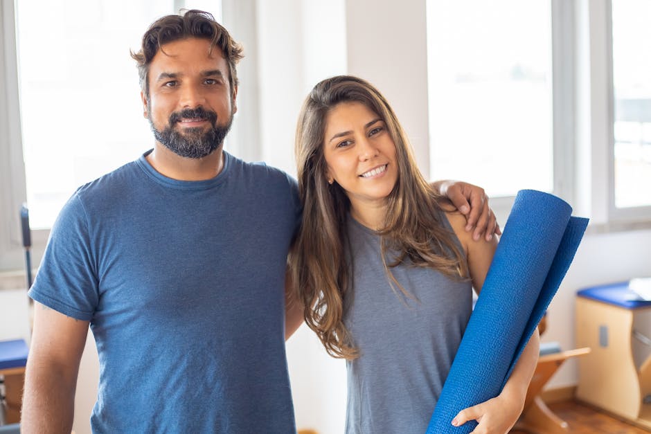 Happy man and woman posing together at gym with a yoga mat, embodying a healthy and active lifestyle.