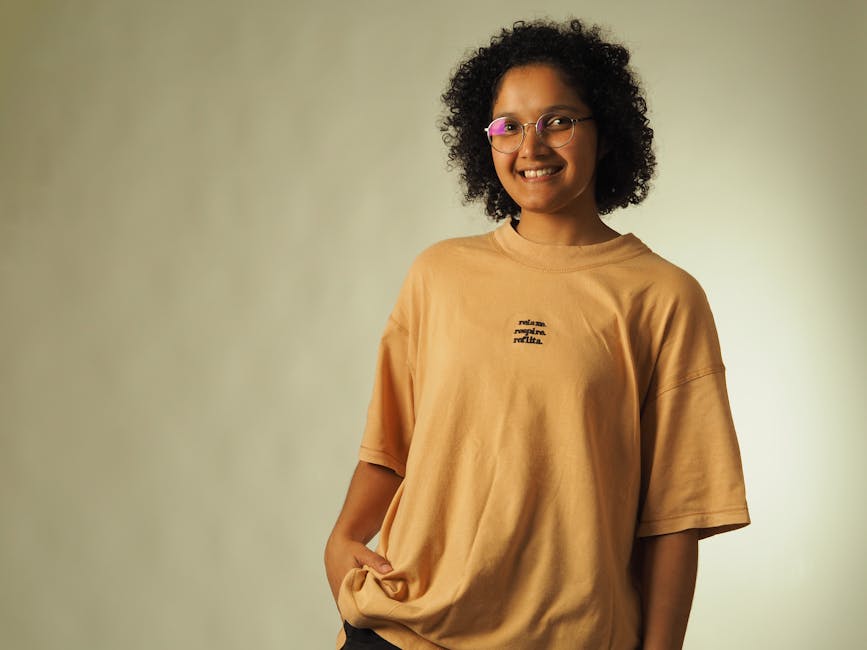A smiling woman wearing glasses and a casual t-shirt poses joyfully.