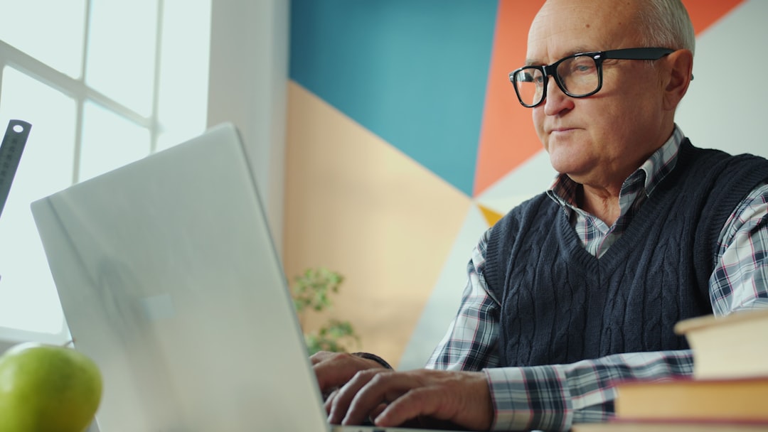 Elderly man with glasses working on a laptop.