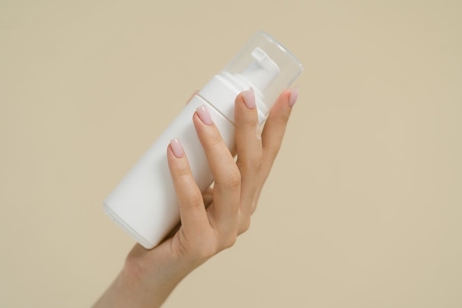 A close-up of a hand holding a white cosmetic bottle against a neutral background, perfect for product mockups and beauty industry use.