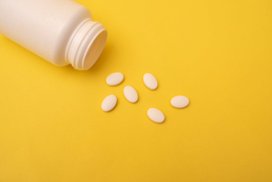 White pills spilling from a plastic bottle on a vibrant yellow background, conveying health and medication themes.