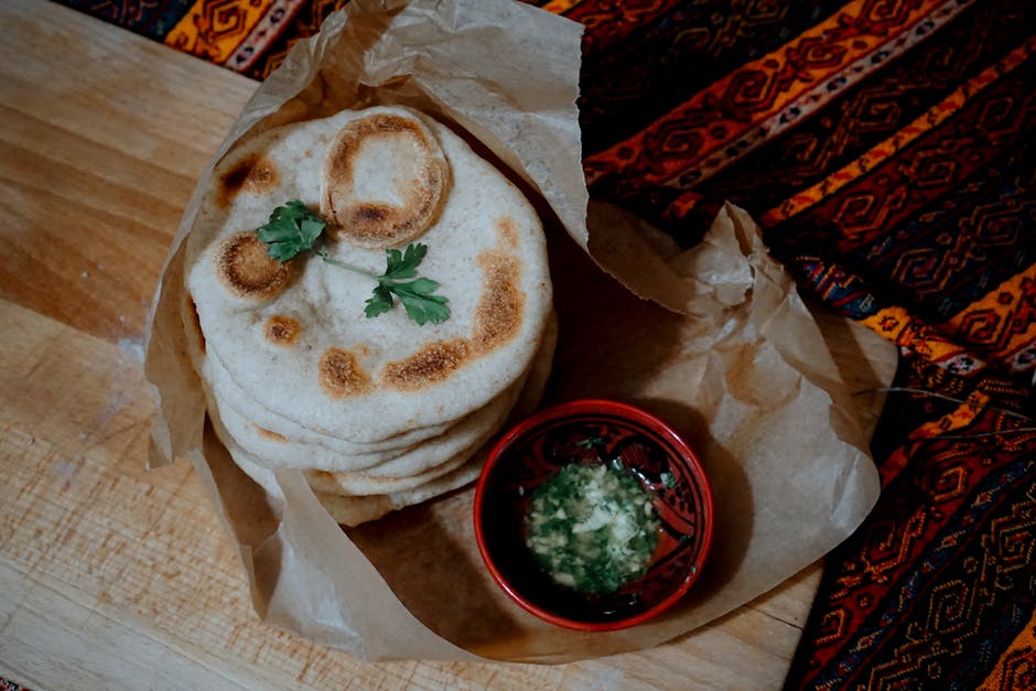 A stack of homemade flatbread with cilantro garnish and a side of herb dip on rustic paper.