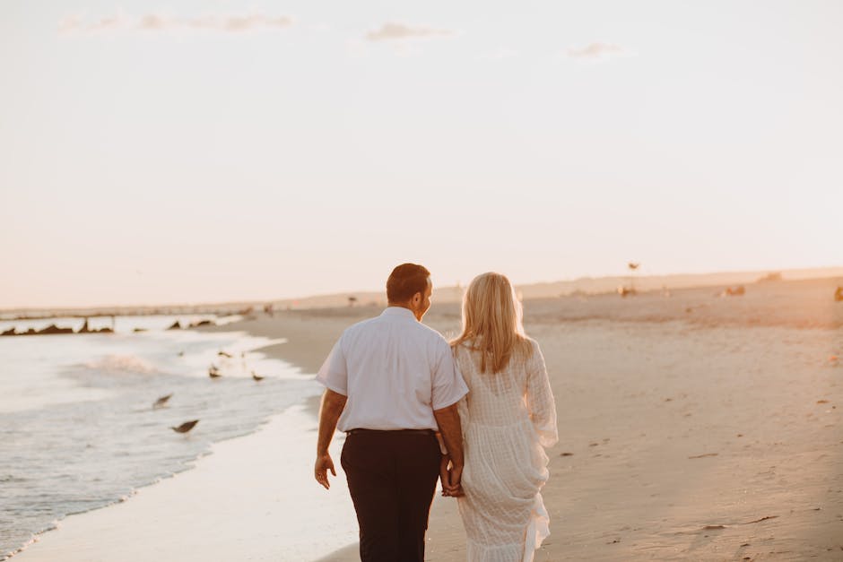 A couple holds hands while walking on a serene beach at sunset, exuding romantic vibes.