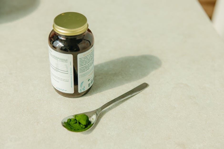 Close-up of a jar and a spoon with green powder, ideal for healthcare and wellness themes.
